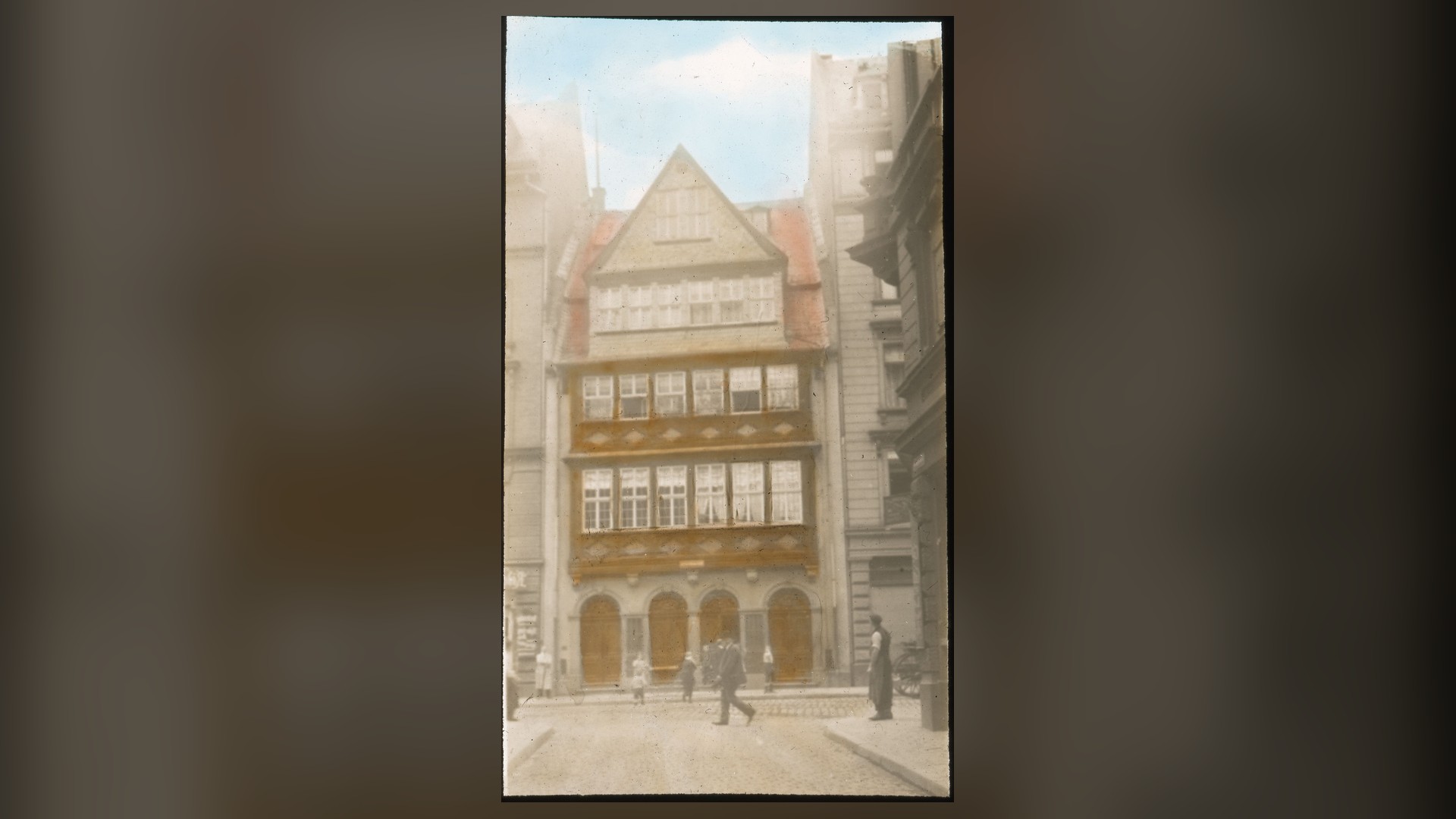 Hand-coloured 1913 photo of the tall, gabled Rothschild family house on a street in Frankfurt's Judengasse.